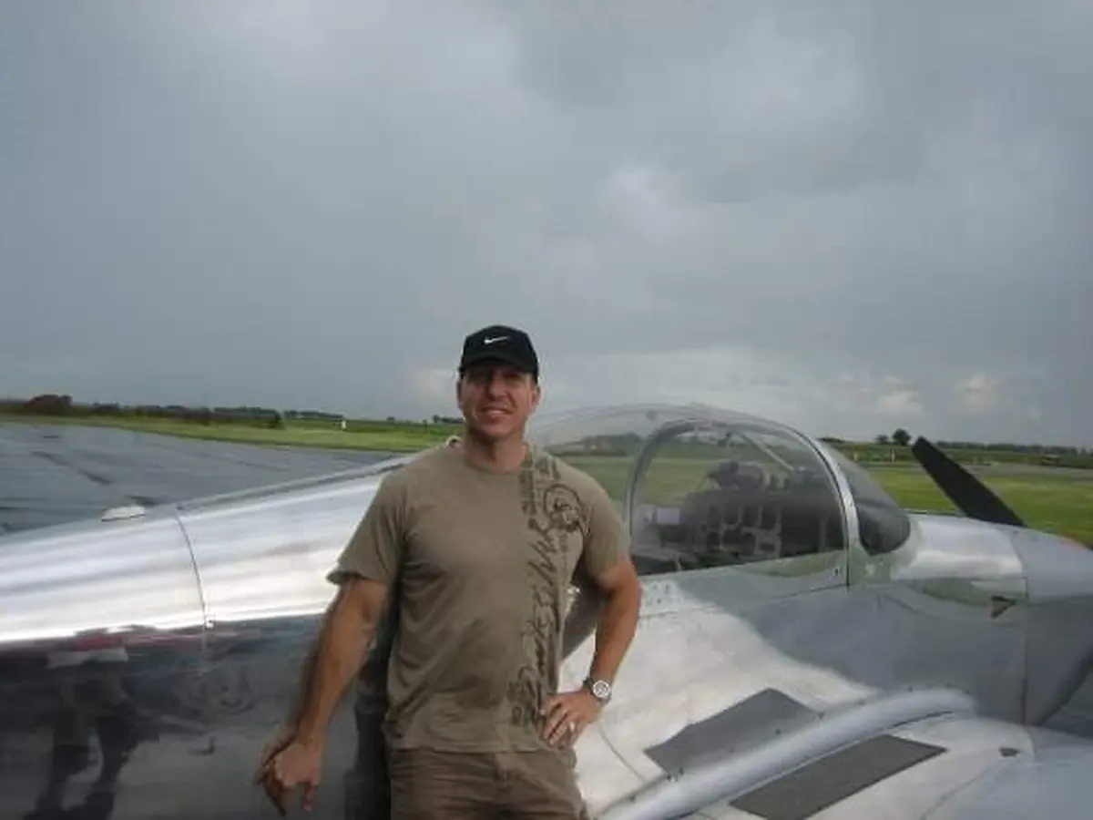 Joseph Joe Helminiak beside a silver light-sport aircraft at an airfield